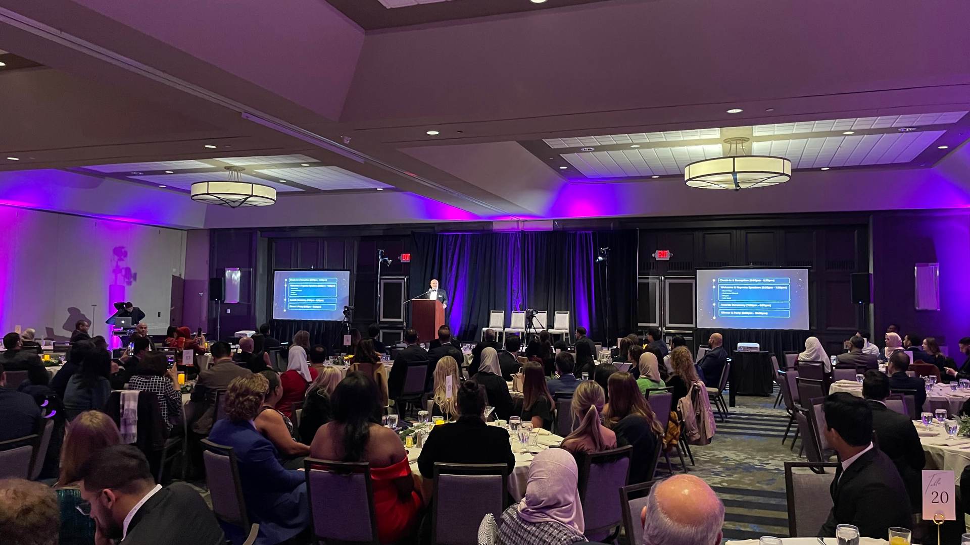 Corporate event AV setup with large projection screen and gold chiavari seating in New Jersey ballroom